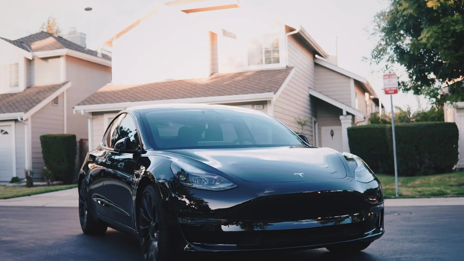 A black sedan parked on a residential driveway in front of a house at dusk