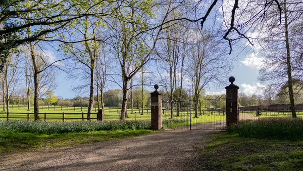 A rural driveway gate between stone pillars opening onto a tree-lined country lane
