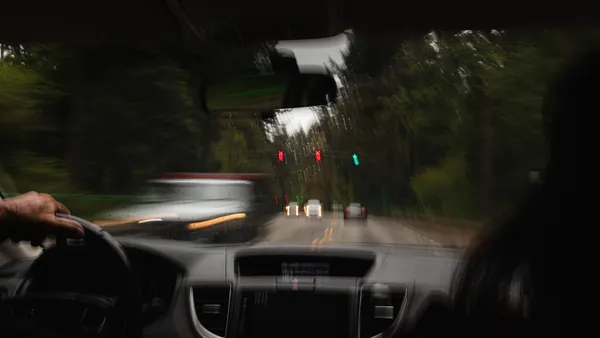 Motion-blurred night drive with a hand on the wheel and traffic lights blurred through the wet windshield