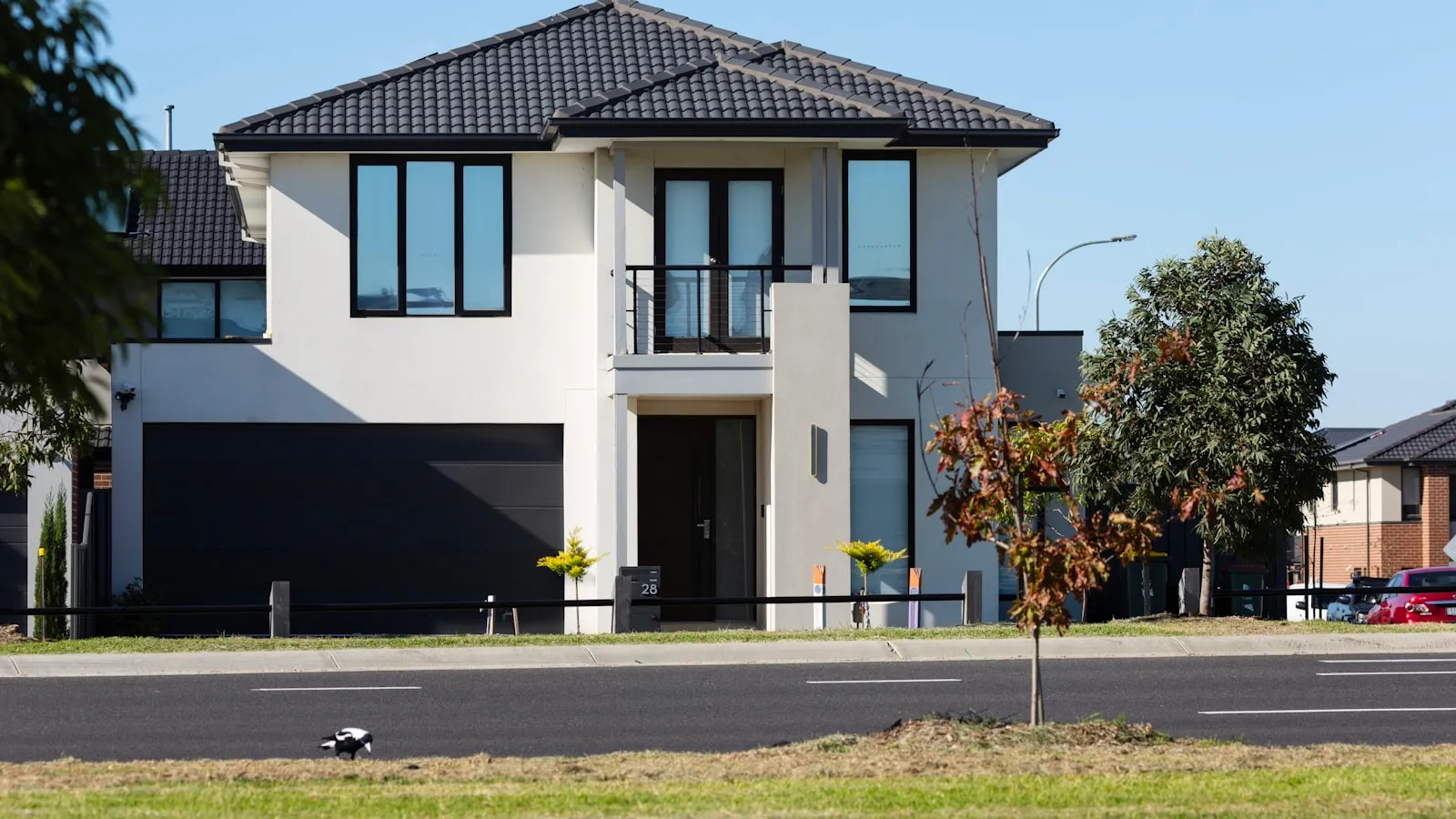 A modern two-story house with a dark double garage door and a small front lawn by the road