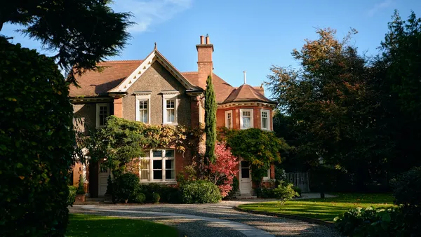 Brick estate house with a curved gravel driveway leading to the entrance, photographed in golden-hour light