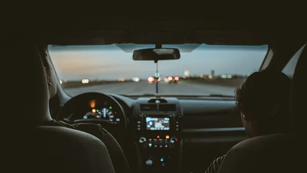 Night car interior view from the back seat showing the center console and windshield with distant traffic lights ahead