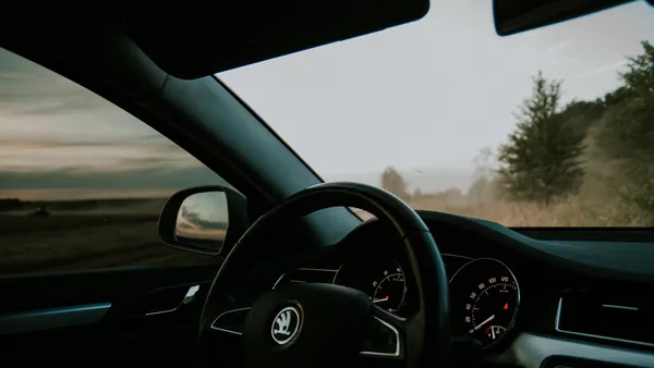 Dashboard and steering wheel of a car with the instrument cluster and green countryside through the windshield