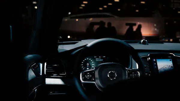 Dark steering wheel and glowing instrument cluster with center touchscreen, blurred showroom lights in background