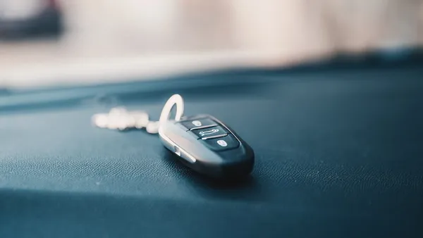 A small black plastic key fob with buttons resting on a dark surface, photographed close-up