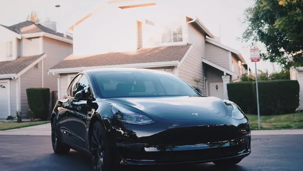 A black Tesla sedan parked in a residential driveway in front of a modern home