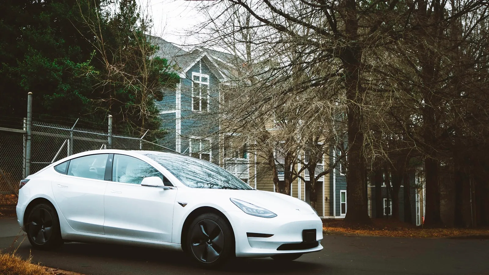 White electric vehicle parked in a residential driveway in front of a house in autumn