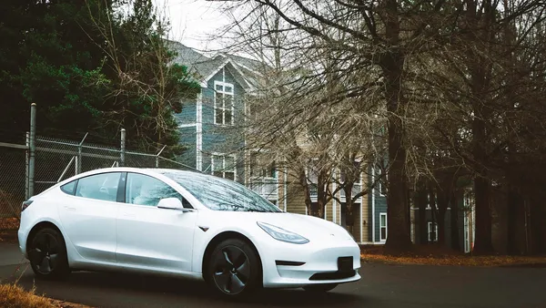 White electric vehicle parked in a residential driveway in front of a house in autumn