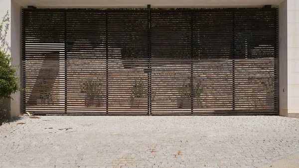 A wide modern horizontal-slat wooden sliding gate across a paved driveway with climbing greenery behind