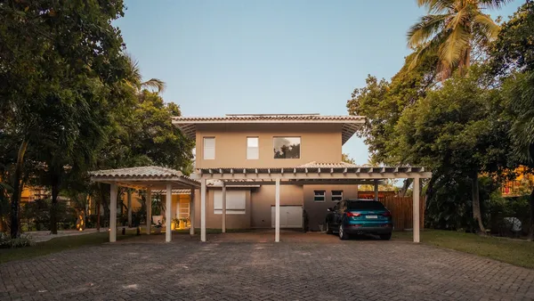 A modern house with a car under a carport at dusk, palms and warm entry lighting