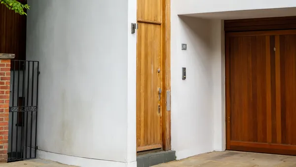 A wooden pedestrian door with an intercom panel beside a wooden garage door and a black wrought-iron side gate
