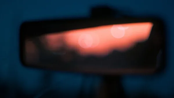 Close-up rear-view mirror glowing red-orange with bokeh, cool blue interior around it