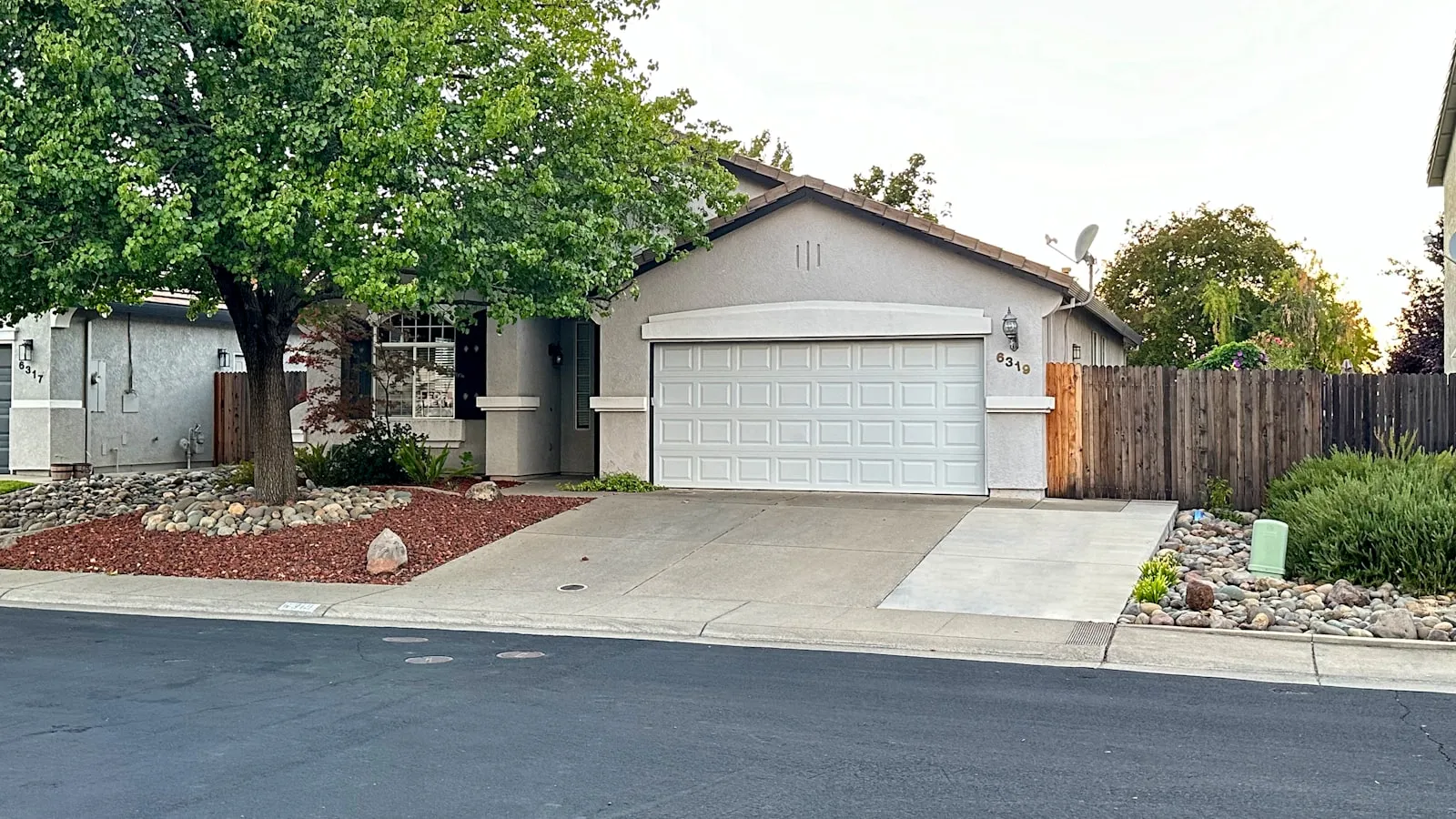 A single-story white house with a two-car garage and a wide driveway, a tree at left