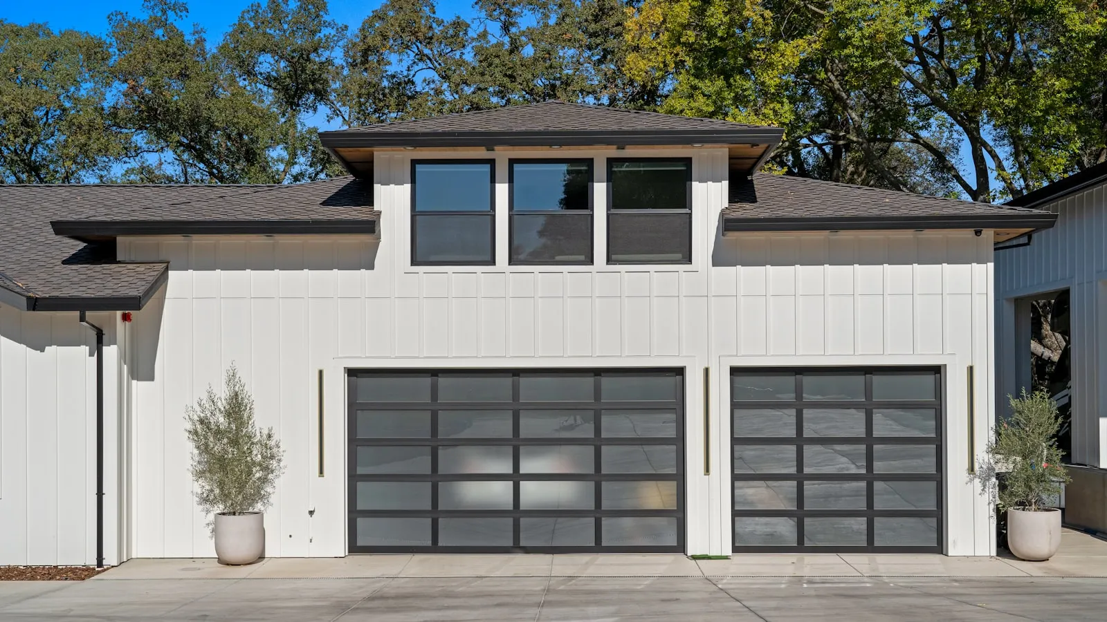 A modern white house with two glass-panel garage doors and potted olive trees