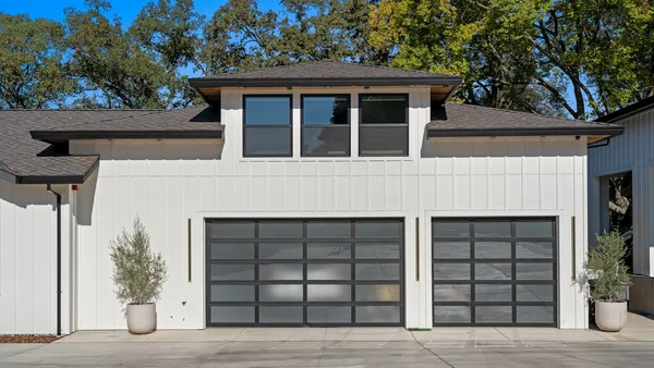 A modern white board-and-batten house with two glass-panel garage doors under a clear blue sky