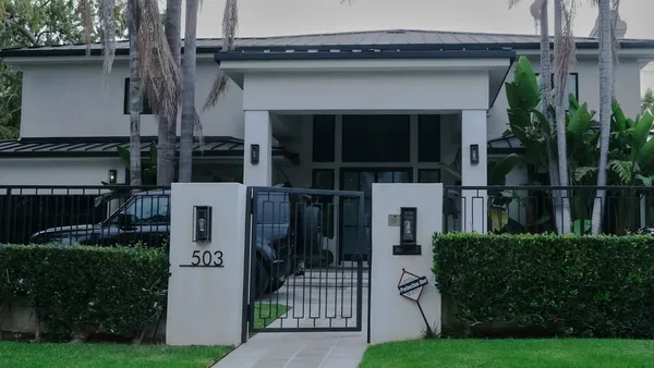 A modern house behind a closed gate with clipped hedges and a dark car parked in the drive
