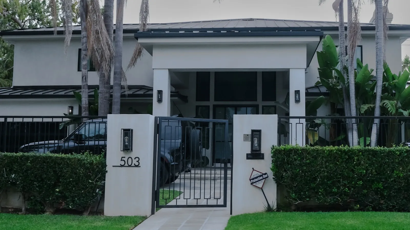 A modern house behind a closed gate with clipped hedges and a dark car parked in the drive
