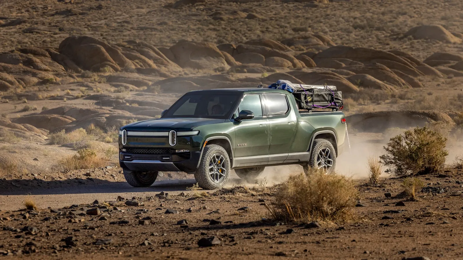 Green Rivian R1T electric pickup truck on a desert trail, dust kicking up behind the rear wheels