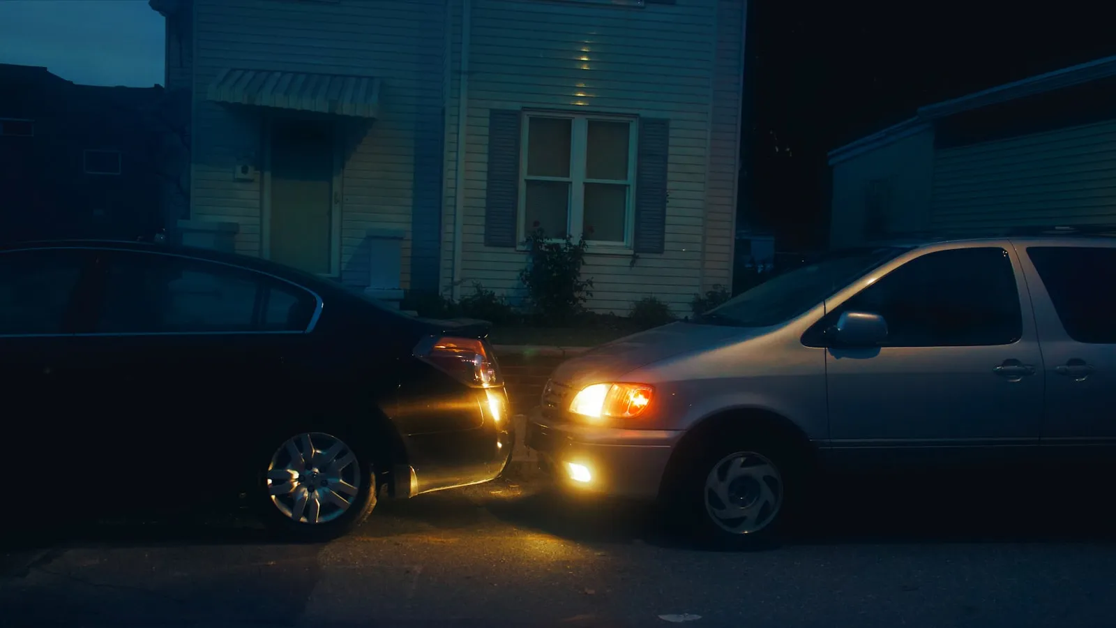 Cars parked in a residential driveway at night, lit by porch lights