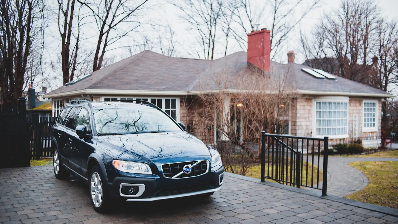 A dark estate wagon in a paver driveway beside a wrought-iron gate