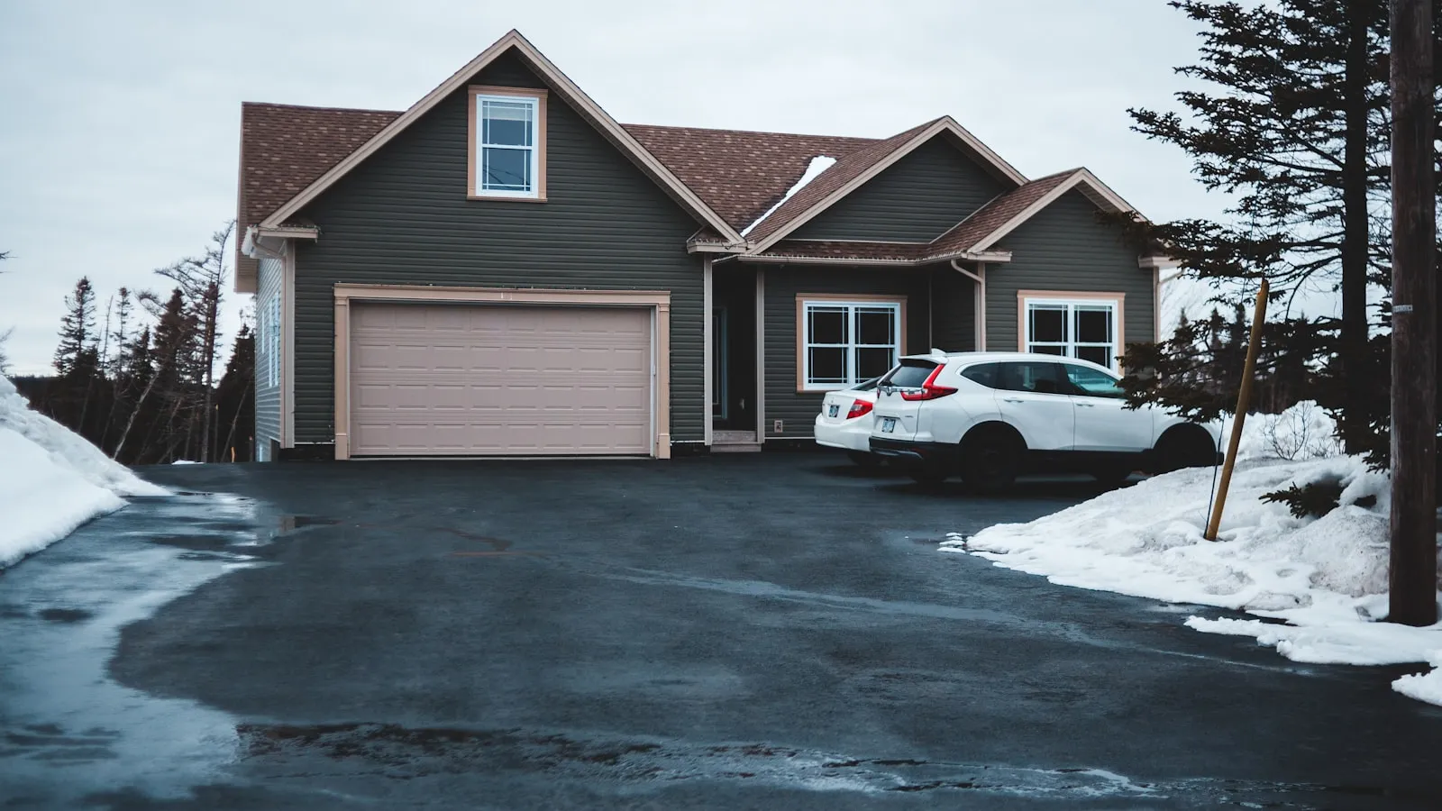 White Honda CR-V parked in a wet driveway in front of a two-car garage on an overcast day