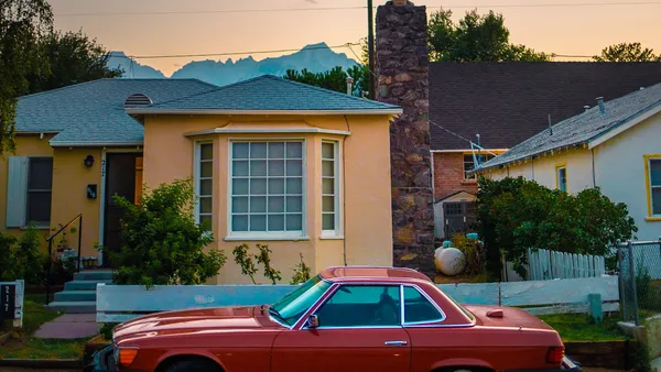 A red vintage Mercedes coupe parked in front of a yellow bungalow with mountains and a warm sunset sky behind