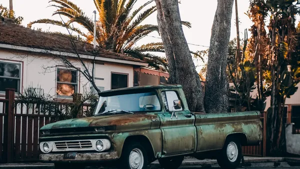 A vintage green pickup truck parked in front of a white house lined with tall palm trees at golden hour