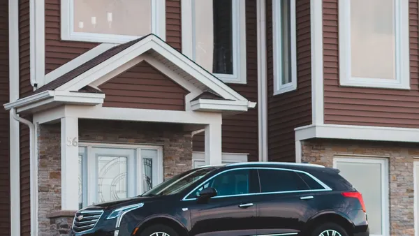 A black Cadillac XT5 SUV parked in front of the covered entrance of a brown-sided house