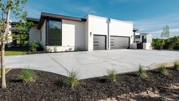 A modern white single-story house with two garage doors and a wide concrete driveway under a blue sky