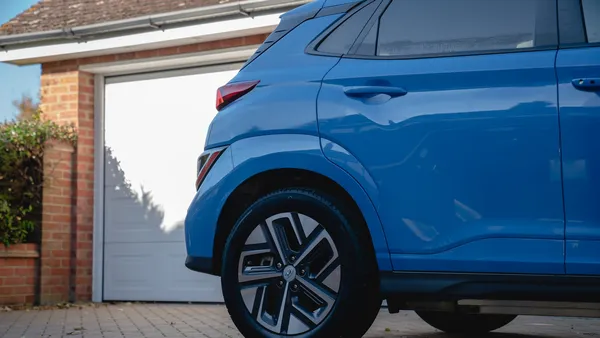 A blue Hyundai Kona Electric on a brick driveway in front of a brick house's white garage door, daylight