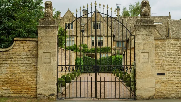 An ornate black wrought-iron gate on red-brick pillars, backed by bare winter trees under an overcast sky